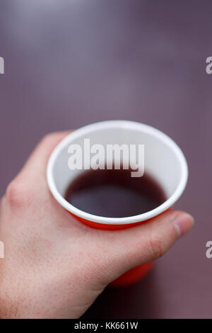 Image de la main de l'homme tenant un plateau avec verre papier rouge sur fond violet floue Banque D'Images