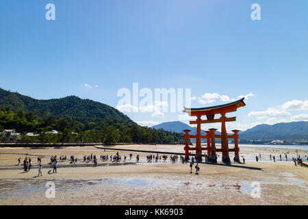 Miyajima - Japon, 26 mai 2017 : rouge torii du sanctuaire d'Itsukushima dans la mer à marée basse près de Miyajima avec beaucoup de touristes la marche sur la san Banque D'Images