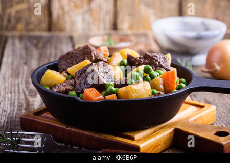 Ragoût de légumes et de boeuf avec des pommes de terre dans la poêle en fonte sur rural tableau Banque D'Images