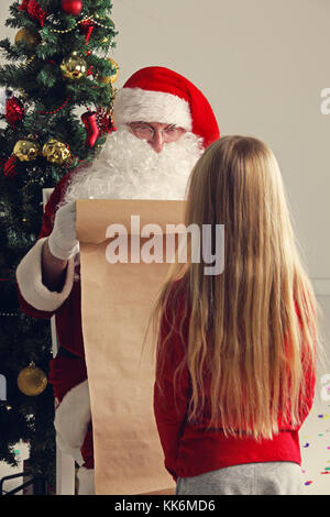 Santa Claus with avec liste ou nice ou naugthy liste papier avec petite fille près de l'arbre de Noël Banque D'Images