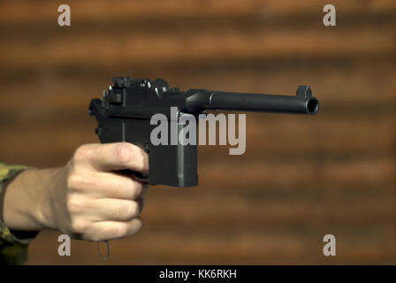 La main d'un homme avec un pistolet semi-automatique vintage pointe au-delà l'image sur l'arrière-plan d'un log mur. L'accent sur le canon du pistolet, le reste je Banque D'Images