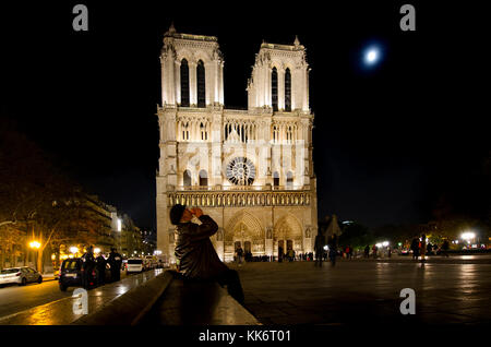 Paris, France. La cathédrale Notre-Dame / Notre-Dame de Paris sur l'île de la Cité. De style gothique. Lit up at night - homme boire un verre Banque D'Images