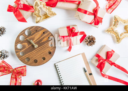 Vue d'en haut vacances de Noël composition avec cadeaux dans du papier craft avec ruban de satin rouge, décor, regarder et ordinateur portable sur le fond en bois blanc avec Banque D'Images