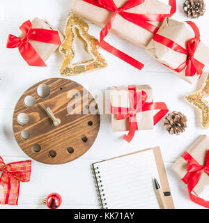 Vue d'en haut vacances de Noël composition avec cadeaux dans du papier craft avec ruban de satin rouge, décor, regarder et ordinateur portable sur le fond en bois blanc avec Banque D'Images