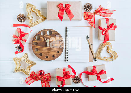 Vue d'en haut vacances de Noël composition avec cadeaux dans du papier craft avec ruban de satin rouge, décor, regarder et ordinateur portable sur le fond en bois blanc avec Banque D'Images