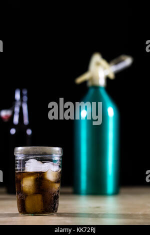 Siphon à soda et un verre de glace et d'orange. la glace avec de la glace sur une table en bois. fond noir Banque D'Images