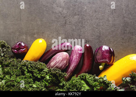 Petite aubergine, courgette jaune, le chou kale et violet le poivre. arrière-plan foncé. La nourriture végétarienne du village Banque D'Images