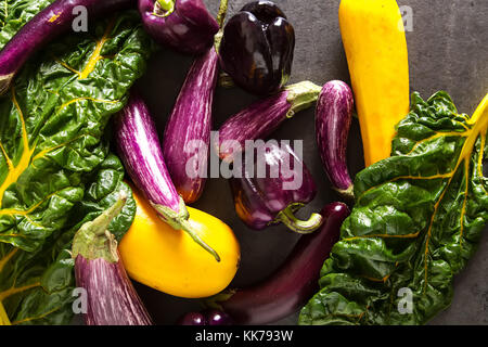 Petite aubergine, courgette jaune et violet, blettes poivre. arrière-plan foncé. La nourriture végétarienne du village Banque D'Images