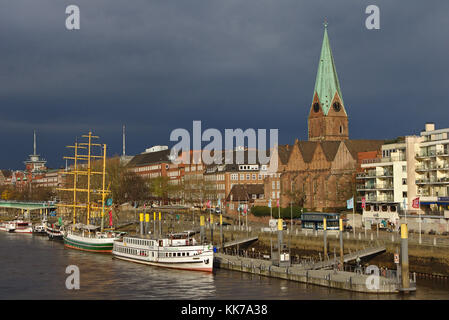 Vue sur le fleuve de Brême, Allemagne avec des navires amarrés, église historique, bâtiments résidentiels et nuages de pluie sombres en arrière-plan Banque D'Images