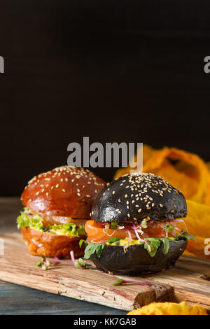 Burger de saumon noir avec du poisson, salade, moutarde. arrière-plan foncé. restauration rapide Banque D'Images