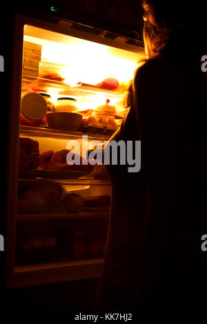 Femme regardant dans réfrigérateur au milieu de la nuit à la recherche de quelque chose à manger. Se concentrer sur un réfrigérateur, image bruitée. Banque D'Images