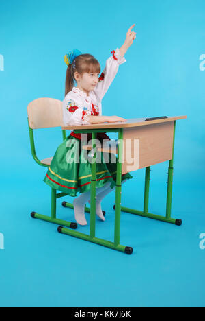 Jeune fille aux cheveux clairs en ukrainien assis sur broderie bureau scolaire isolé sur fond bleu Banque D'Images