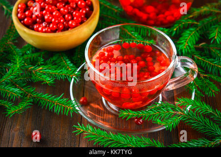 Le thé chaud à partir de la canneberge dans une tasse en verre entouré de branches de sapin sur une table en bois Banque D'Images
