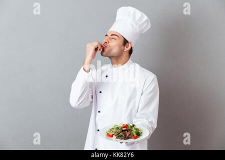Portrait of a handsome male chef habillés en uniforme avec la plaque sur fond gris isolé plat Banque D'Images