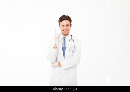 Portrait of a young male doctor with stethoscope habillés en uniforme et permanent du doigt jusqu'isolé sur fond blanc Banque D'Images