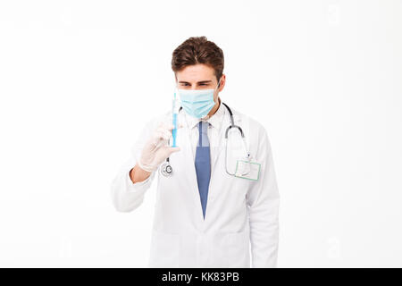 Close up portrait of a male doctor with stethoscope habillés en uniforme et mask holding a syringe isolated over white background Banque D'Images