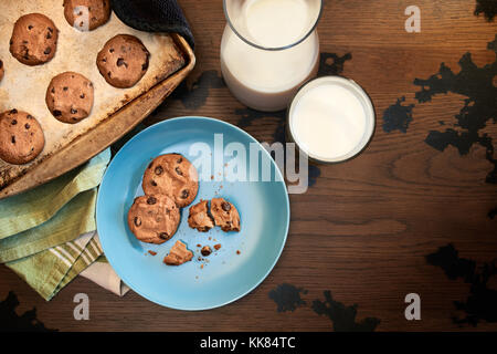 Vue de dessus de la plaque à biscuit et de cookies aux pépites de chocolat chaud du four avec un verre de lait froid sur table en bois vintage Banque D'Images