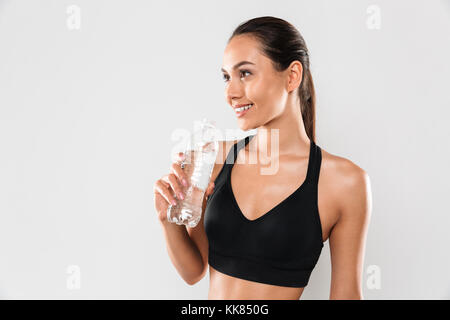 Photo de happy young woman posing isolé sur fond gris. À côté de l'eau potable. Banque D'Images