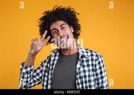 Portrait of a cheerful casual homme africain à la caméra et au geste de paix montrant plus isolé sur fond orange Banque D'Images