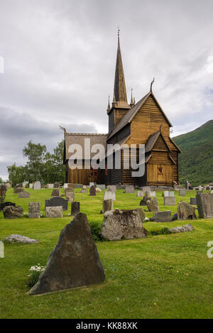 L'ancienne église de douves de bois de lom, datant du xiie siècle avec des pierres tombales sur le cimetière en face d'elle en Oppland, Norvège. Banque D'Images