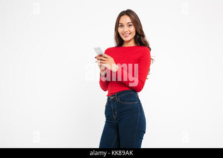 Portrait of a smiling attractive asian woman texting on mobile phone while isolés sur fond blanc Banque D'Images