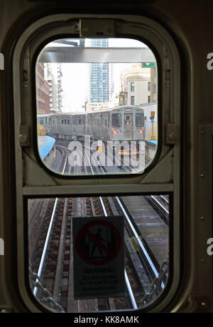 Une ligne brune train voyageant au nord est encadré par la fenêtre de la dernière voiture sur un autre train en direction sud dans le Chicago's Loop. Banque D'Images