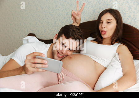 Drôle de jeunes femmes enceintes en couple tout en selfies Lying in Bed Banque D'Images