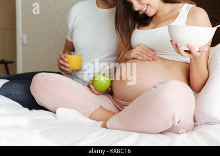 Portrait d'une jeune femme enceinte couple having healthy breakfast ensemble tout en restant assis dans le lit Banque D'Images