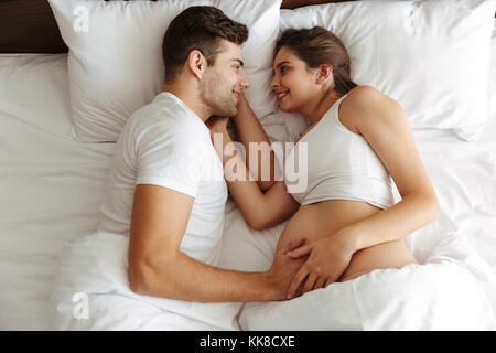 Image femme enceinte à l'intérieur à la maison se trouve au lit avec son beau charmant mari. Banque D'Images