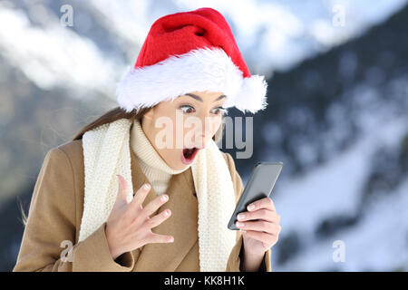 Surpris girl en ligne news à Noël avec la montagne enneigée en arrière-plan Banque D'Images