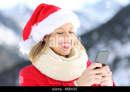 Happy girl sur vacances de Noël à l'aide de smart phone avec la montagne enneigée en arrière-plan Banque D'Images