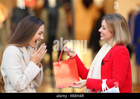 Vue latérale d'un client heureux de donner un cadeau à un ami en hiver sur la rue dans un centre commercial Banque D'Images