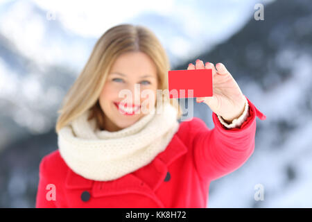 Vue avant, portrait d'une femme montrant une carte de crédit en hiver avec la montagne enneigée en arrière-plan Banque D'Images