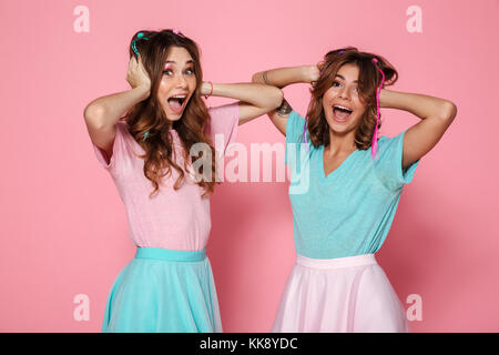 Portrait de deux jeunes filles joyeuses habillés en vêtements colorés et crier à la caméra au plus isolé sur fond rose Banque D'Images