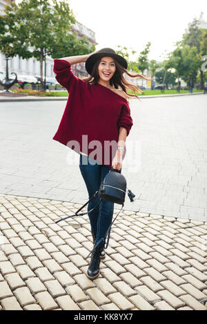 Portrait d'une jeune femme asiatique joyeux habillés en pull et chapeau la marche à l'extérieur Banque D'Images