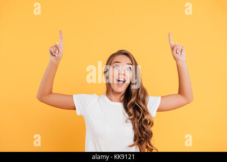 Photo de heureux surpris belle jeune femme debout et posant sur fond de mur isolé jaune. À la caméra et soulignant copyspace. Banque D'Images