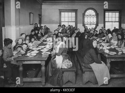 Une photographie d'un groupe important de femmes et d'enfants de manger un repas sur Ellis Island, le long de tables en bois sont très proches d'accommoder le plus de gens possible dans cette salle à manger, des repas gratuits sont offerts aux immigrants et les marchandises emballées sont également disponibles pour la vente de manger entre les repas et pour les immigrants de s'emporter quand ils ont quitté l'Ellis Island, New York, 1907. À partir de la Bibliothèque publique de New York. Banque D'Images