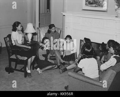 Une photo de jeunes femmes rencontre avec un instructeur de l'Administration nationale de la jeunesse, ils sont réunis dans un salon, certaines des jeunes femmes s'asseoir sur le sol car il n'y avait pas assez de sièges pour tout le monde, l'NYA était une organisation formée dans le cadre du New Deal de Franklin Roosevelt, l'objectif de l'Agence consistait à fournir une formation et des emplois pour les Américains âgés entre 16 et 25 ans, elle a fonctionné de 1935 à 1939, cette réunion a eu lieu au Centre communautaire Bon Pasteur à Chicago, Illinois, 1877. À partir de la Bibliothèque publique de New York. Banque D'Images