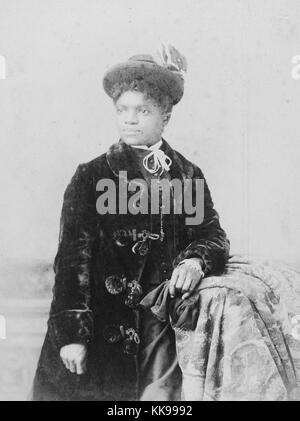 Une longueur de trois quarts photographique portrait d'une femme non identifiée, elle porte un long manteau de velours, et un chapeau, elle s'appuie sur une grande table recouverte de tissu, 1900. À partir de la Bibliothèque publique de New York. Banque D'Images