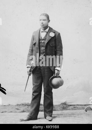 Sepia studio portrait d'un homme afro-américain, pleine longueur, d'un costume, tenant un chapeau melon et canne à sucre, 1900. À partir de la Bibliothèque publique de New York. Banque D'Images