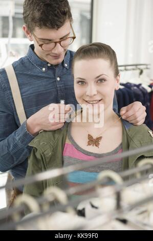 Jeune homme mettant collier autour du cou de la jeune femme au magasin de mode | utilisation dans le monde entier, libre de droits : pour le prix d'utilisation comercial sur demande. Banque D'Images