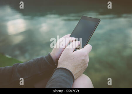 Femme à l'aide de téléphone mobile à l'extérieur dans la nature. femmes avec le smartphone par le lac taper le texte du message. Banque D'Images