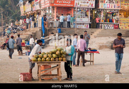 Les hommes vendent des noix de coco en face de stands de nourriture rapide sur la plage de Juhu, Mumbai, Inde Banque D'Images