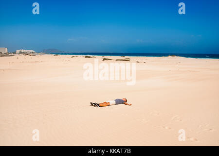 Un jeune caucasien portant un t-shirt et un short se trouve avec ses bras ouverts sur le sable blanc des dunes de Corralejo à Fuerteventura, île des Canaries Banque D'Images