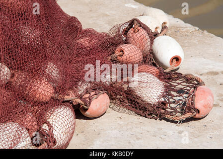 Les filets de pêche en nylon rouge séchant au soleil sur le côté du port Banque D'Images