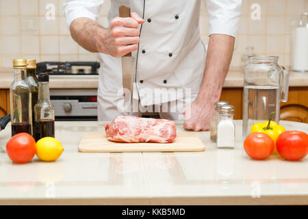 Couper la viande de boucherie sur planche, cuisinier professionnel tenant le couteau et couper la viande. Banque D'Images