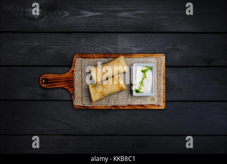 Crêpes farcies mince ou fédération de blinis avec de la crème. sur une planche de bois. Vue du haut fond de bois noir. Banque D'Images