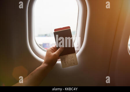 Main tenant passeport avec avion de retour sur la fenêtre plan fond ensoleillé Banque D'Images