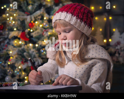 Enfant écrit lettre père noël. Une petite fille avec enthousiasme attire. Chambre des décorations de Noël, Christmas Tree Banque D'Images