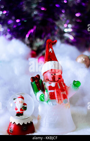 Jouets mignon de snowman in santa hat avec don et le père Noël en boule de cristal sur fond neigeux floue flou artistique avec tresse. Banque D'Images